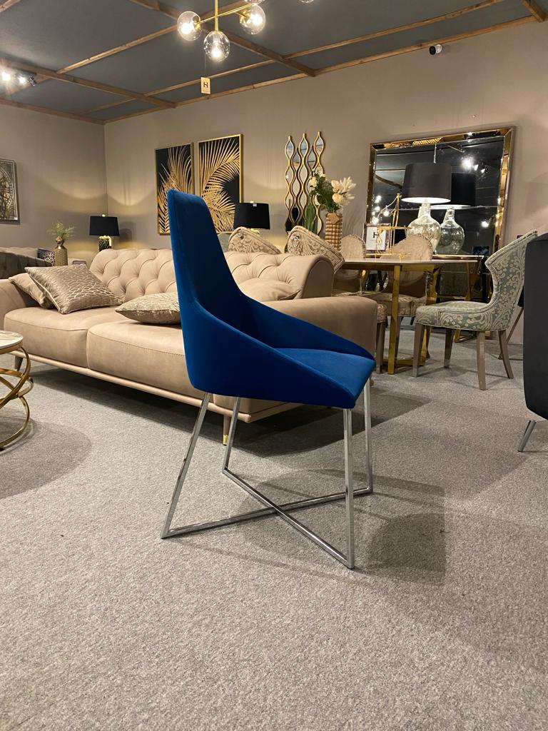 A furniture showroom featuring a sofa, artwork, mirrors, and a blue chair with a metallic frame in the foreground, alongside an elegant set of Home Signature Venice Dining Chair in Blue Colour.